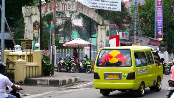 Micolet pasando por la entrada de un barrio de Ambon, donde esperan algunos Ojet (moto-taxis) 